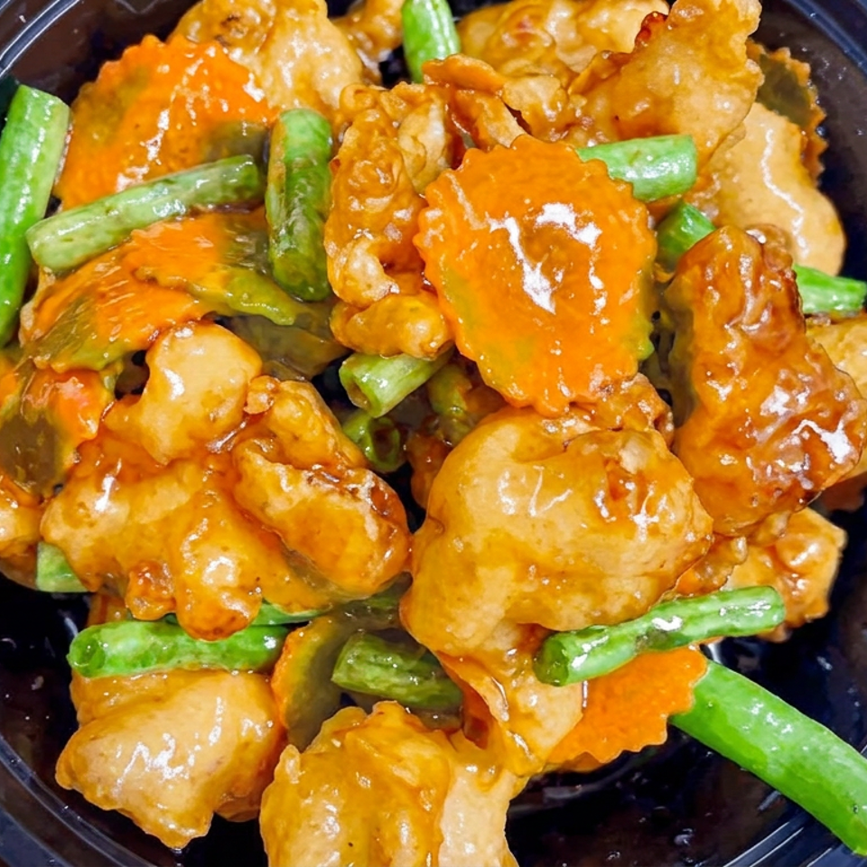 Close-up of saucy battered chicken with green beans and sliced carrots in a black serving bowl.